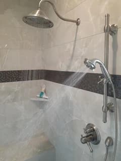 Chrome shower controls and handheld shower fitted to a tiled wall