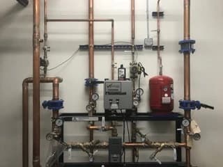 Wall-mounted mechanical piping with pumps, valves, and an expansion tank
