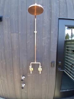 Copper outdoor shower and exposed piping against dark siding