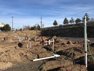Plumbing lines and vertical pipe risers across an excavated construction site