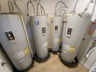 Multiple water heaters installed side by side with overhead connections